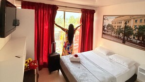 A hotel room with a bed, a desk, a TV, and a window with red curtains. - Hotel Toledo FL (Cartagena)