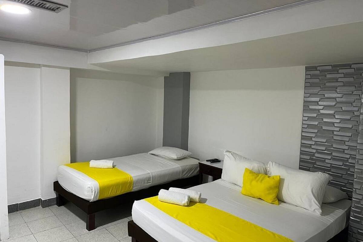 A hotel room with two beds, each with white bedding and yellow accents.