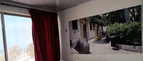 Une chambre à coucher avec un grand lit, une table de chevet, une fenêtre avec des rideaux rouges et un tableau accroché au mur.