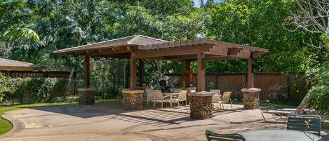 A covered outdoor patio with stone pillars, wooden chairs, and a table.