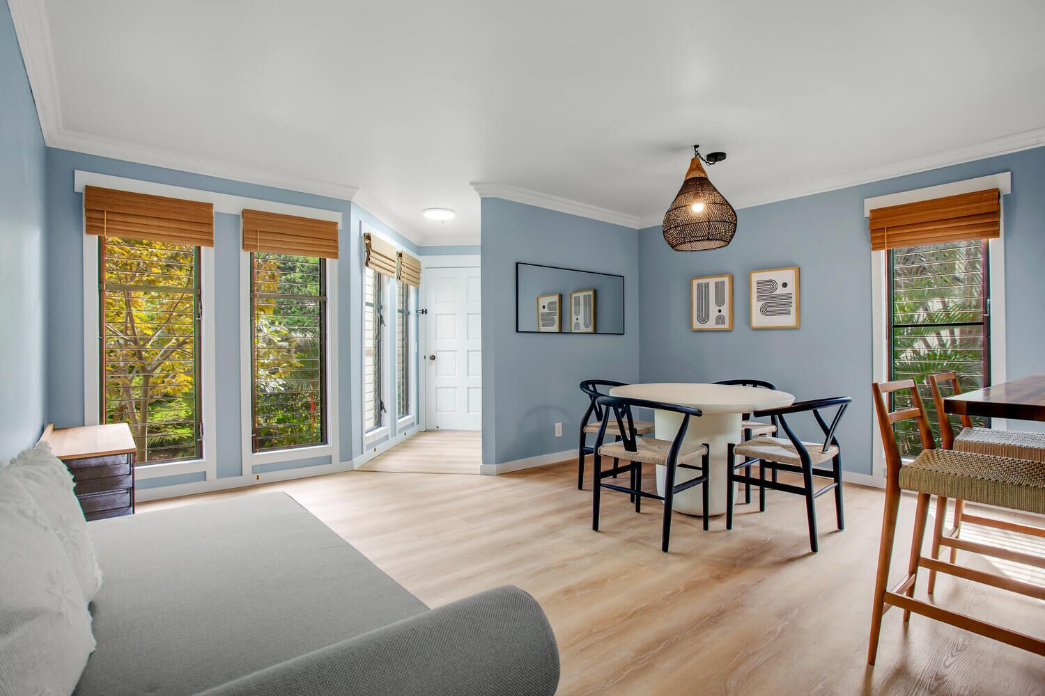 Une pièce comprenant un lit, une table à manger avec des chaises et de grandes fenêtres équipées de stores.