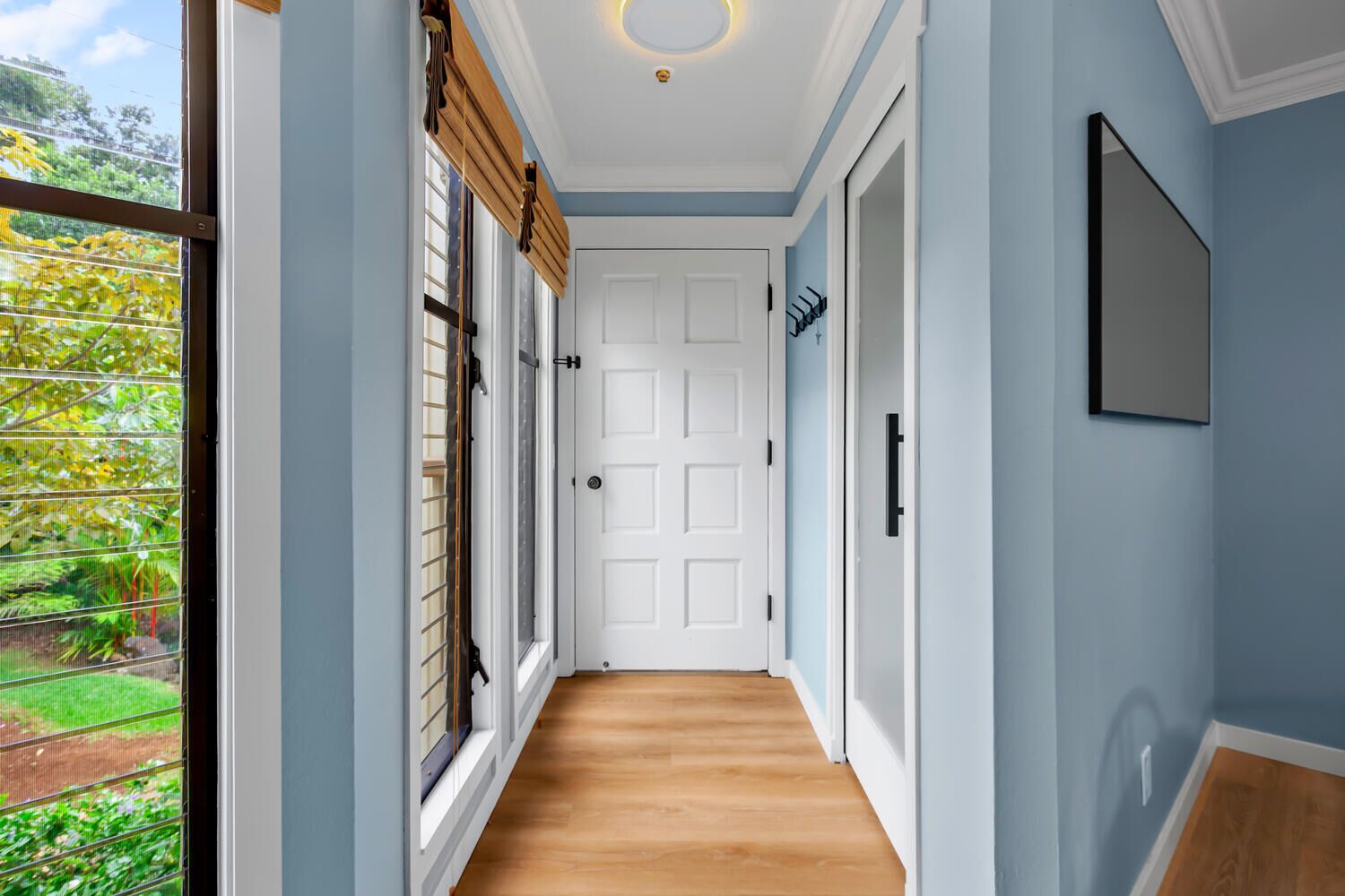 Un pasillo con paredes azul claro, suelo de madera y una puerta blanca al final.