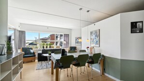 Un saló modern amb un sofà, taula de dinar i cadires. Hi ha plantes en testos i obra d'art a les parets.