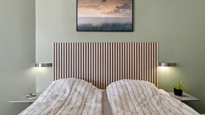 Un dormitori amb un llit, una tauleta de nit, un quadre penjat a la paret i una làmpada de nit.