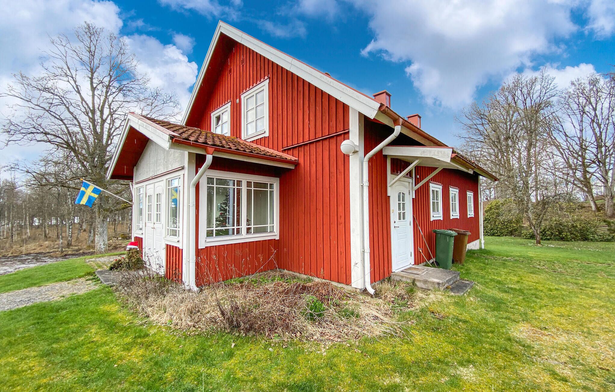 A red wooden house with white trim, a small front porch, and a flag.