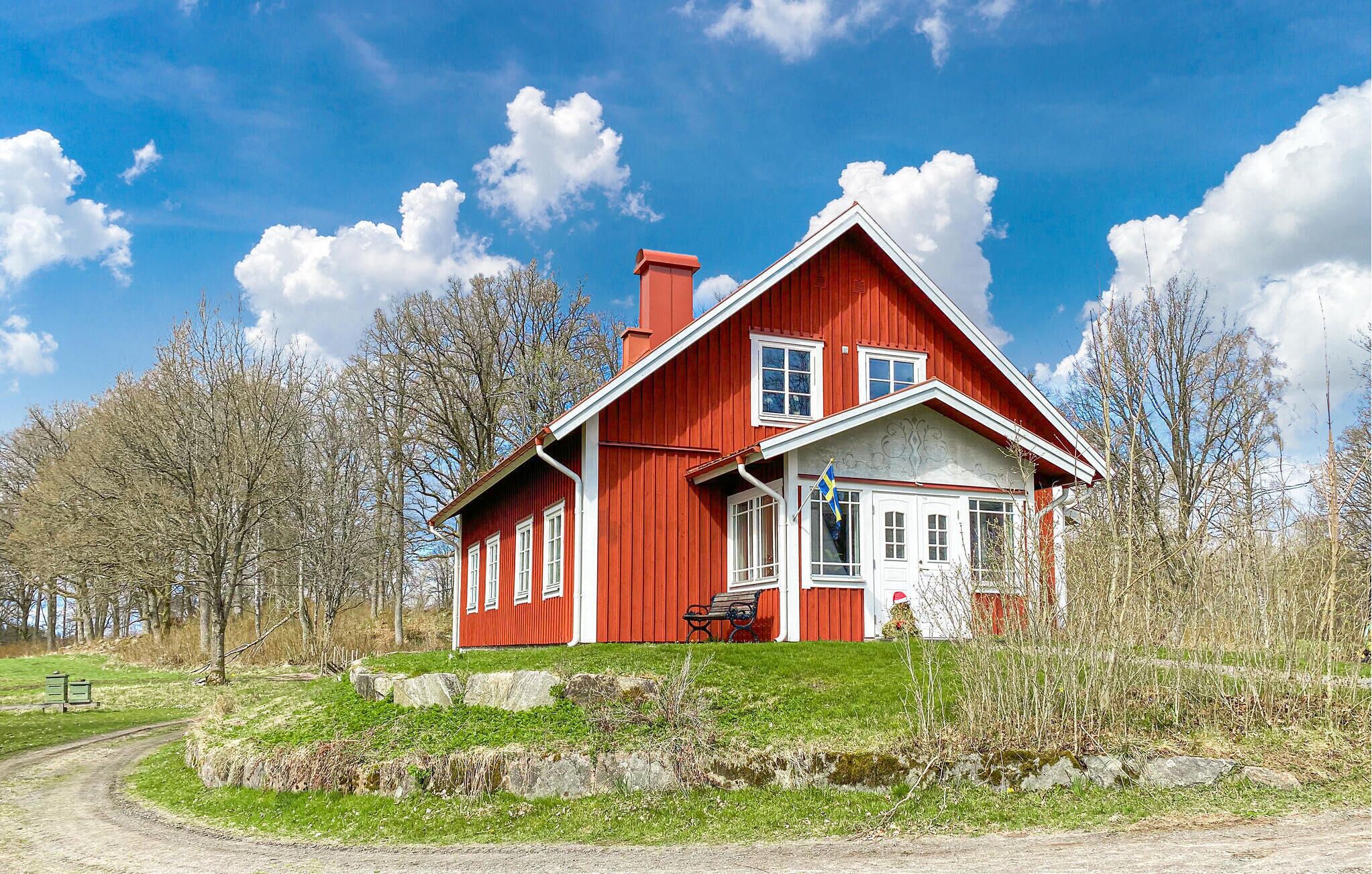 Una casa de madera roja con puerta y ventanas blancas, rodeada de árboles y un área con césped.