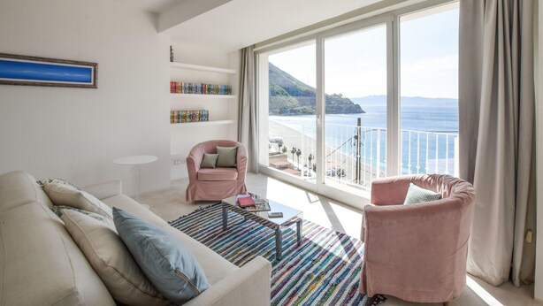 Een woonkamer met een bank, fauteuil en uitzicht op zee.