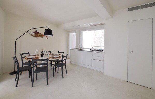 A modern kitchen with white cabinets, a dining area with four chairs, and a large window providing natural light. - Beach front home in Scilla with WiFi (Scilla)