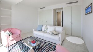 Een moderne woonkamer met een witte bank, een roze fauteuil, een glazen salontafel en een grote garderobe.
