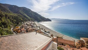 Een kustplaats met terracotta daken, een strand en een bergachtige achtergrond.