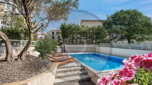 Piscina com espreguiçadeiras, uma palmeira e degraus que levam à piscina.