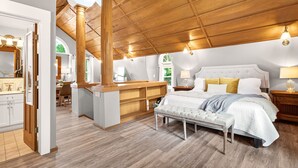 A spacious bedroom with a large bed, wooden ceiling beams, and a view of greenery outside. - Downtown, 6 kings, Sleeps 14+, Game Room,  Courtyard, Hot Tub (Colorado Springs)
