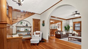 A spacious living room with a wooden staircase, a white armchair, a leather sofa, and a ceiling fan. - Downtown, 6 kings, Sleeps 14+, Game Room,  Courtyard, Hot Tub (Colorado Springs)
