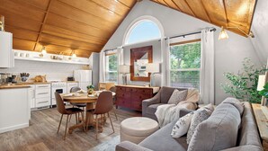 A modern kitchen with white cabinets, a dining area with a round table and chairs, and a living room with a grey sofa and ottoman. - Downtown, 6 kings, Sleeps 14+, Game Room,  Courtyard, Hot Tub (Colorado Springs)