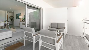 Un salon moderne comprenant un canapé, des fauteuils, une table basse et une porte vitrée donnant sur un espace cuisine.