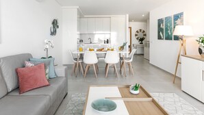 Un salon moderne avec un canapé gris, une table basse et un coin repas comprenant une table et des chaises blanches.