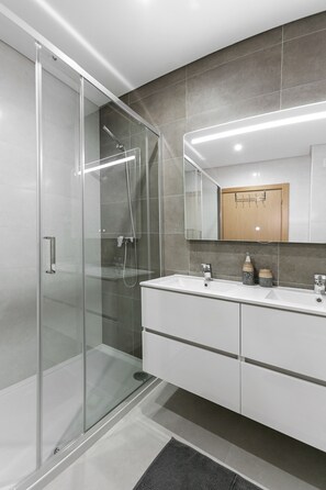 A modern bathroom with a glass-enclosed shower, a vanity with a mirror, and a wooden cabinet above the sink. - Zahra Place - Shared Pool (Nazaré)