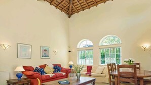 A spacious living room with a high wooden ceiling, two sofas, a dining table, and large windows offering a view of greenery. - Attractive Family Villa, A/C, Private Pool - 5mins drive to the Iconic Beach at Praia da Marinha! (Lagoa)
