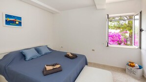 A bedroom with a bed, pillows, a window with a view of flowers, and a painting on the wall. - 3 bedroom beautiful apartment in Klek (Klek)