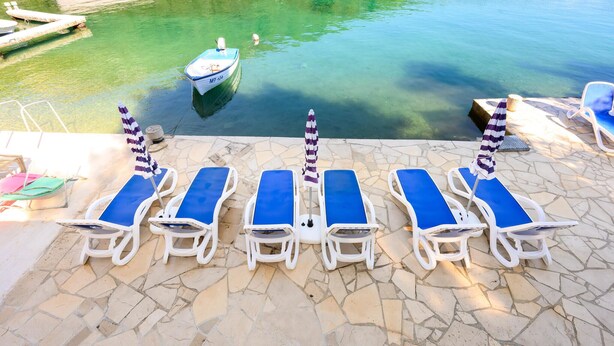 A poolside area with lounge chairs and umbrellas, a small boat, and a clear view of the water. - 3 bedroom beautiful apartment in Klek (Klek)