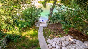 A stone pathway leading to a dock over a calm body of water, surrounded by lush greenery. - 3 bedroom beautiful apartment in Klek (Klek)
