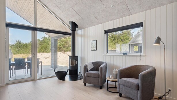 Ein modernes Wohnzimmer mit Kamin, zwei Sesseln, einem kleinen Tisch und einem großen Fenster mit Blick ins Freie.