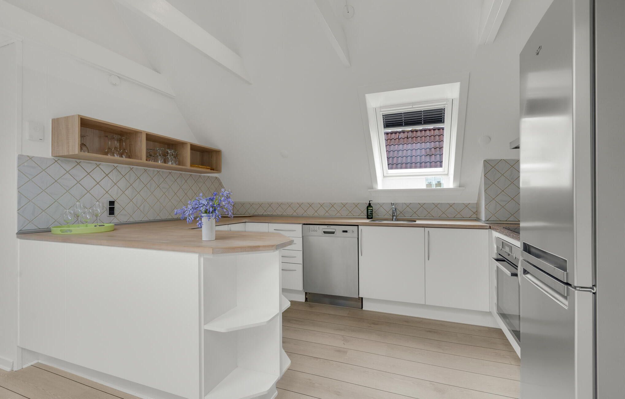 A modern kitchen with white cabinetry, a wooden countertop, a built-in dishwasher, and a stainless steel refrigerator.