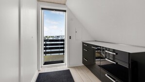 Una habitación moderna y compacta con puerta corredera a un balcón, un mueble negro y un ventanal pequeño.