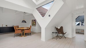 Un loft espacioso con techo alto, un comedor con mesa y sillas de madera, una pequeña zona de estar con una silla, y un tragaluz.