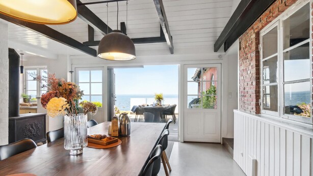 Un coin repas avec vue sur la mer, comprenant une table en bois, des chaises et un vase rempli de fleurs.