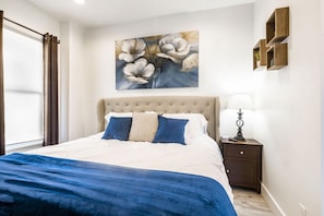 A bedroom with a large bed, a nightstand, a lamp, and a painting of flowers on the wall.