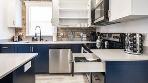 Una cocina moderna equipada con lavavajillas, estufa y microondas. Se aprecia una ventana con persianas, un lavaplatos y una encimera con diversos utensilios de cocina.