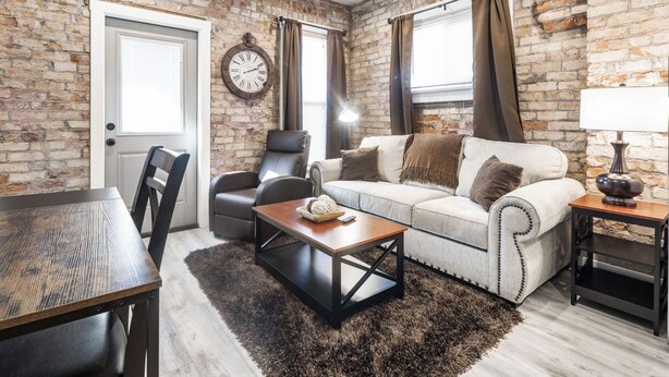Una sala de estar acogedora con pared de ladrillo, un sofá, un sillón, una mesa de centro y una lámpara.