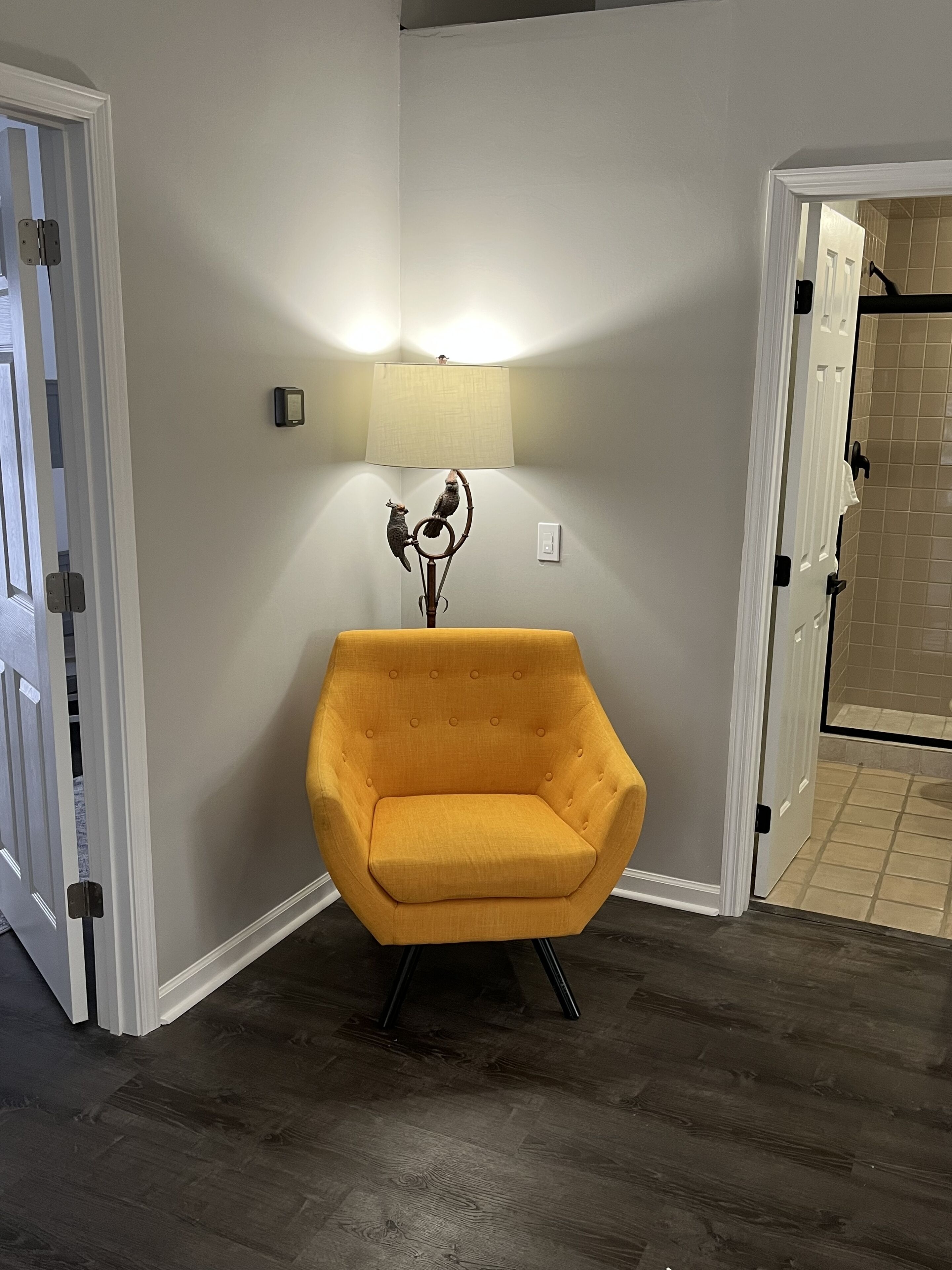 Una habitación de esquina con un sillón amarillo, una lámpara de pared y una puerta que da a un baño.