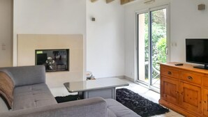 A living room with a grey sofa, a small table, a wooden cabinet, and a TV. - Amazing home in Erquy with heated swimming pool (Erquy)