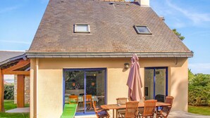 A house with a sloped roof, two skylights, a covered patio with a table and chairs, and a sliding glass door. - Amazing home in Erquy with heated swimming pool (Erquy)