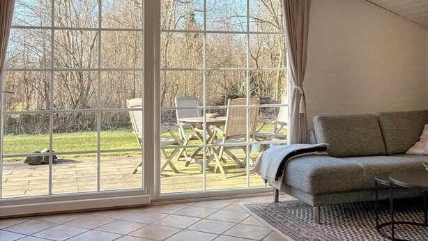 A room with a grey sofa, a small table, and a view of an outdoor patio with chairs and a table. - Gorgeous home in Hemmet with WiFi (Hemmet)
