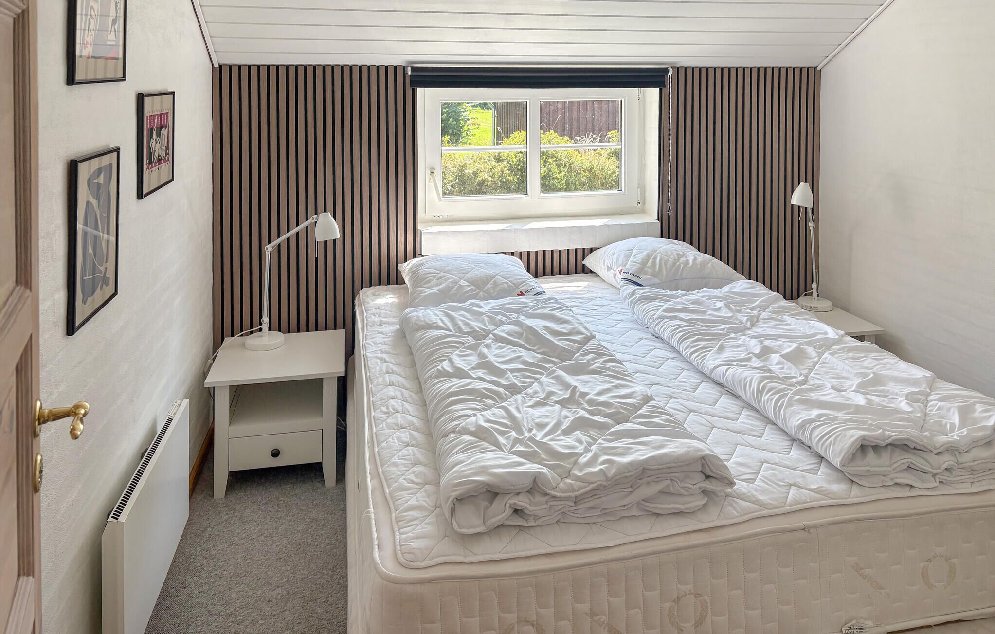 Un dormitorio con una cama, dos mesitas de noche, una ventana y un radiador.