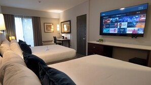 Habitación de hotel con dos camas, un escritorio, un televisor mostrando un canal de cine y una ventana con cortinas.