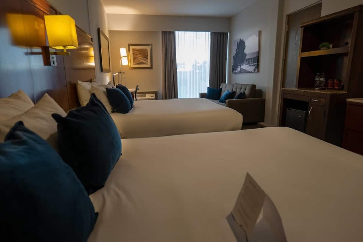 A hotel room with two beds, a desk, a chair, and a small kitchenette.