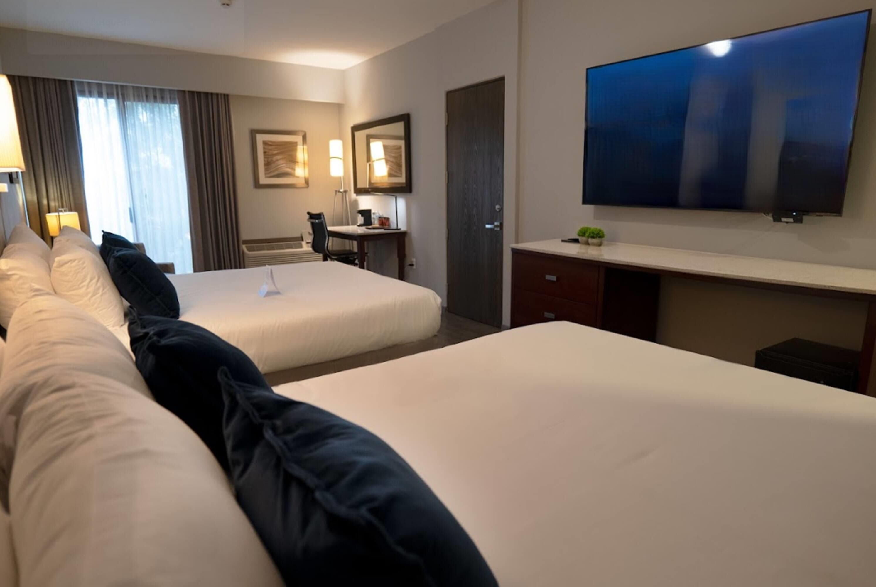 Una habitación de hotel con dos camas, un escritorio, una silla, un televisor y una puerta.