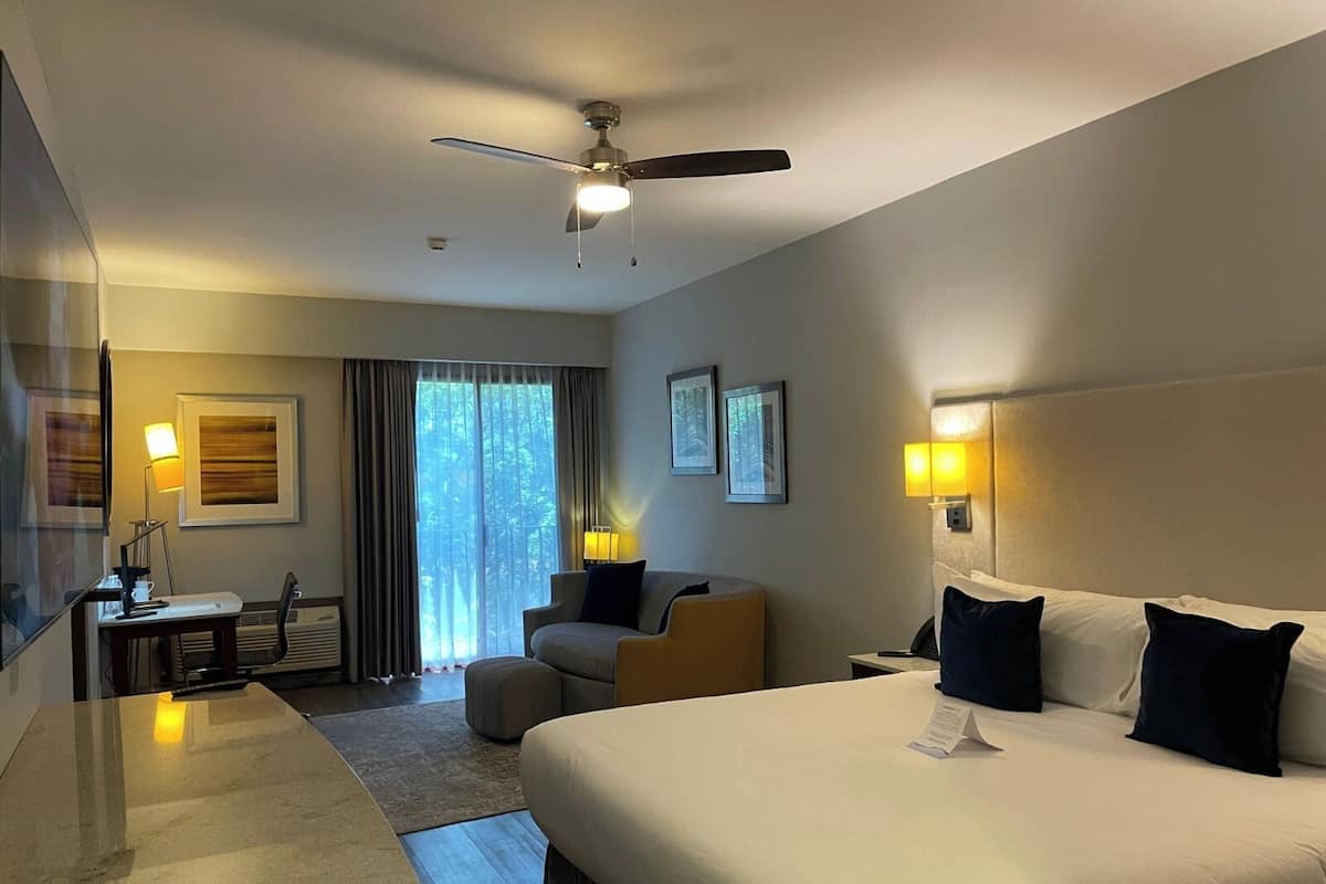 A hotel room with a large bed, a desk, a chair, and a ceiling fan.
