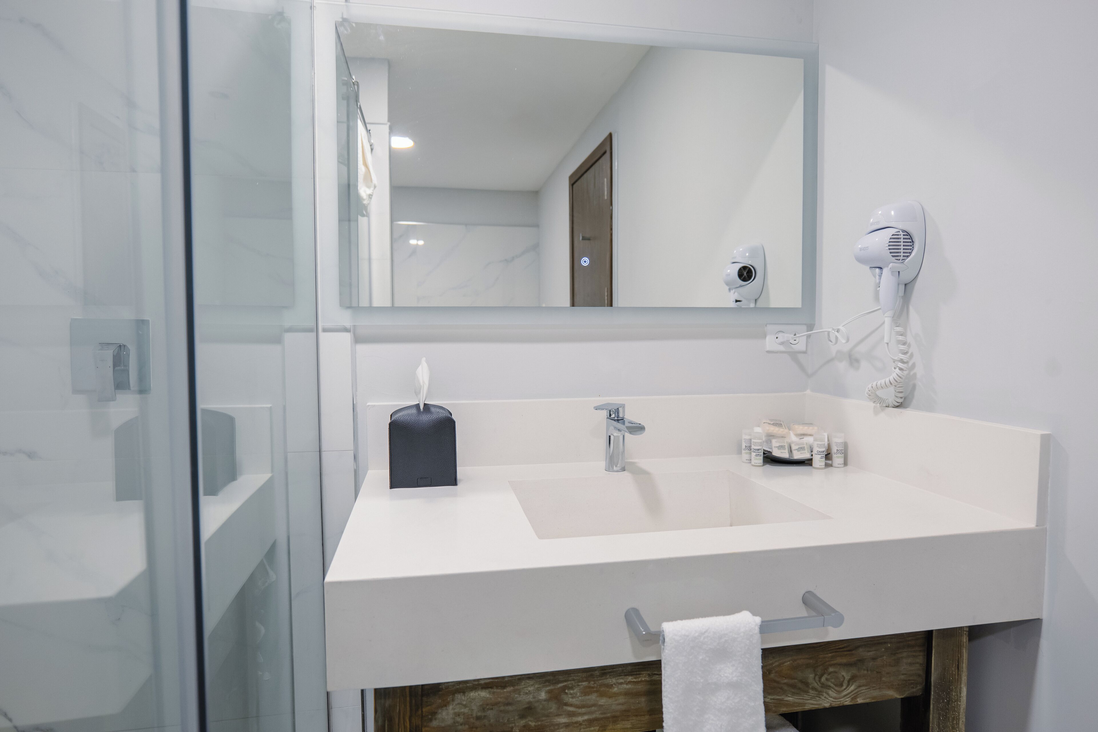 A modern bathroom with a white sink, a mirror, a hairdryer, and toiletries.