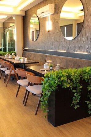 Een restaurant met een lange toonbank, meerdere stoelen en een decoratieve wand met spiegels en planten.