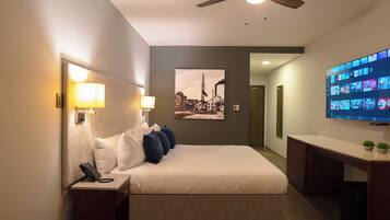 A hotel room with a bed, bedside lamps, a desk, a television, and a ceiling fan.
