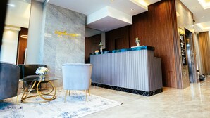 Un área de recepción moderna con pared de mármol, mostrador de recepción y una zona de estar con una mesa redonda y sillas.