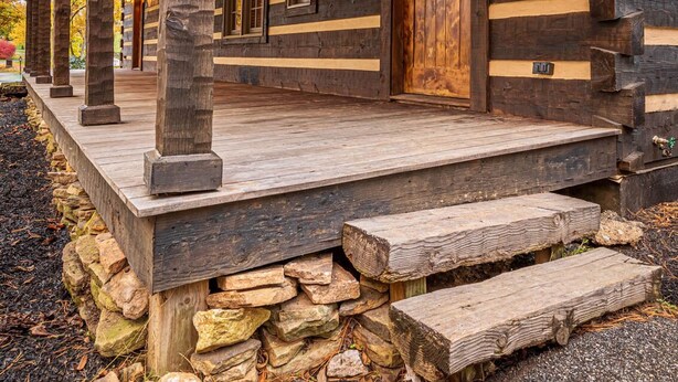 A log cabin with a wooden porch, stone foundation, and a large wooden door. - The Log House at Twin Brook (Gap)