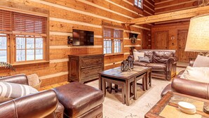 A log cabin interior with leather furniture, a flat-screen TV, and a fireplace. - The Log House at Twin Brook (Gap)