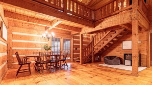 A spacious wooden cabin interior with a dining area, staircase, and a cozy seating area. - The Log House at Twin Brook (Gap)