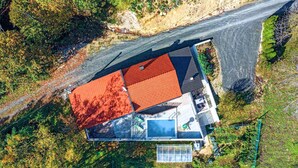 Vista aérea de una casa con techo rojo, un amplio ventanal y un patio cercado.
